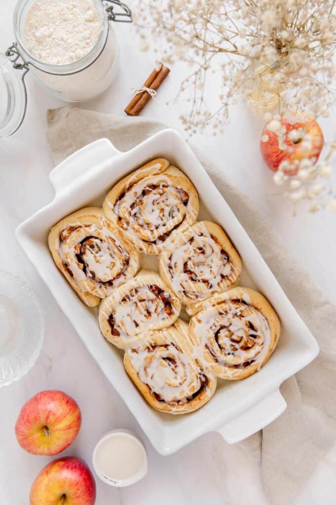 Vegan cinnamon rolls drizzled with icing in a baking dish.