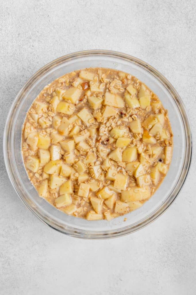 Apples folded into the oatmeal mixture in a glass bowl.