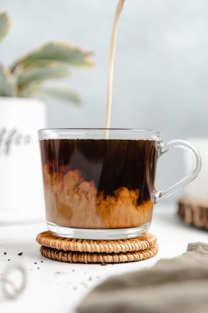 Creamer being poured into a glass coffee mug.