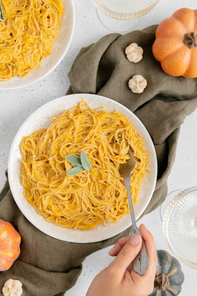 A hand twirling vegan pumpkin pasta on a fork.