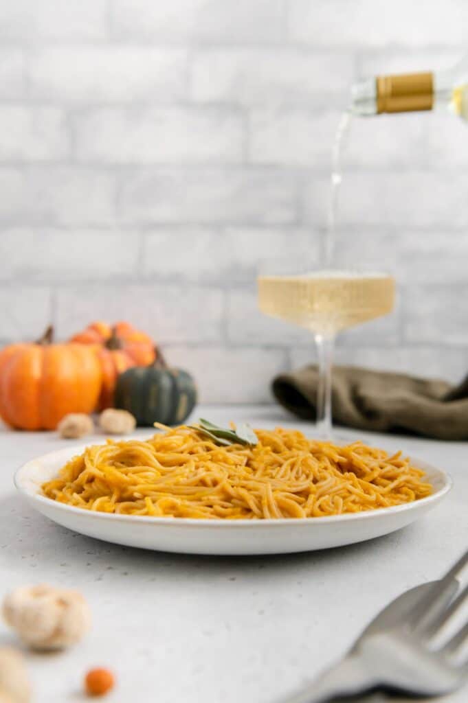 White wine being poured in the background with pumpkin pasta in the foreground.
