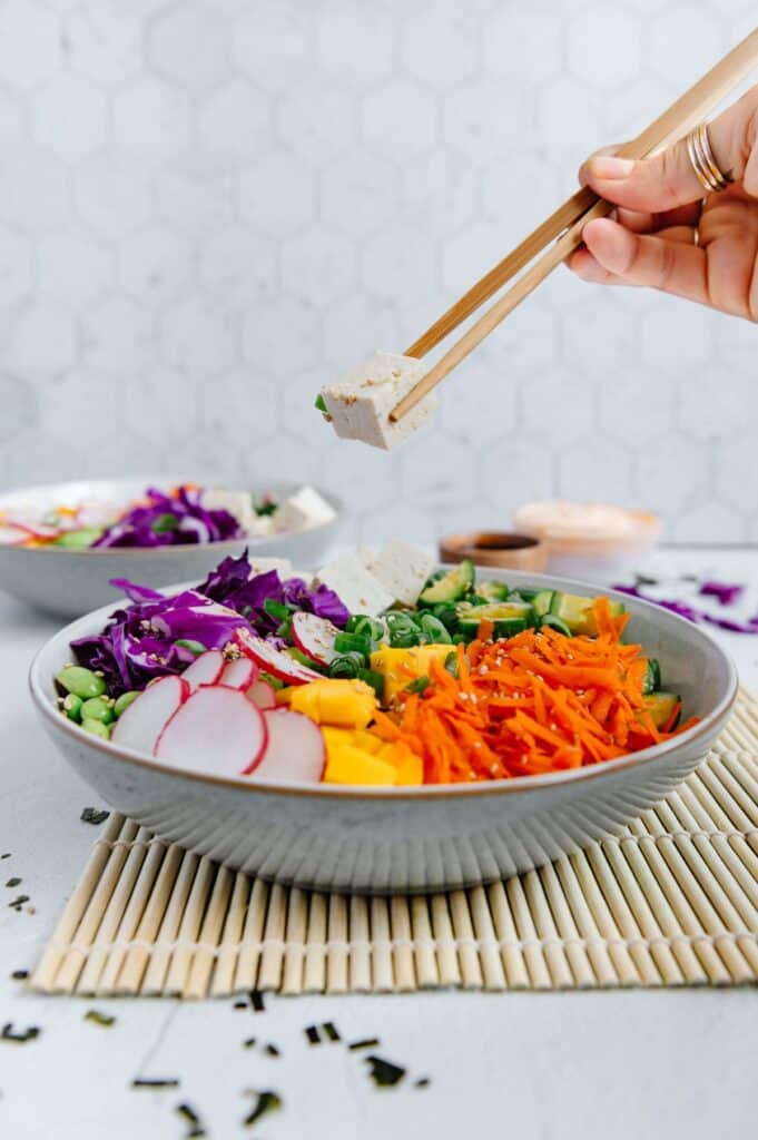Chopsticks holding a piece of sliced tofu over a tofu poke bowl.
