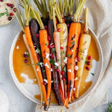 Rainbow carrots garnished with vegan feta, pomegranates, and parsley.