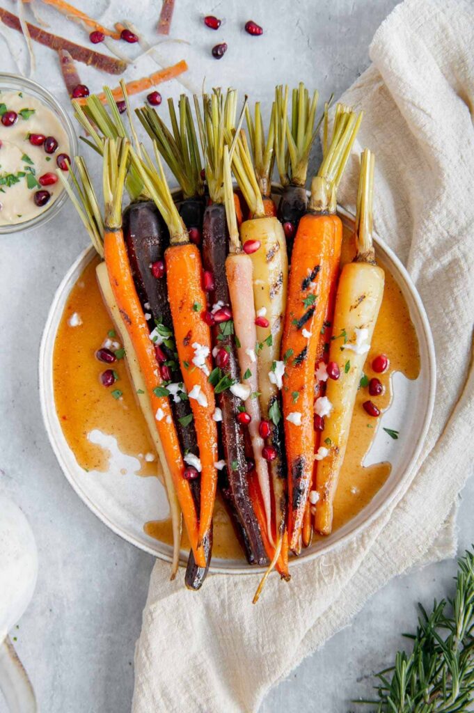 Rainbow carrots garnished with vegan feta, pomegranates, and parsley.