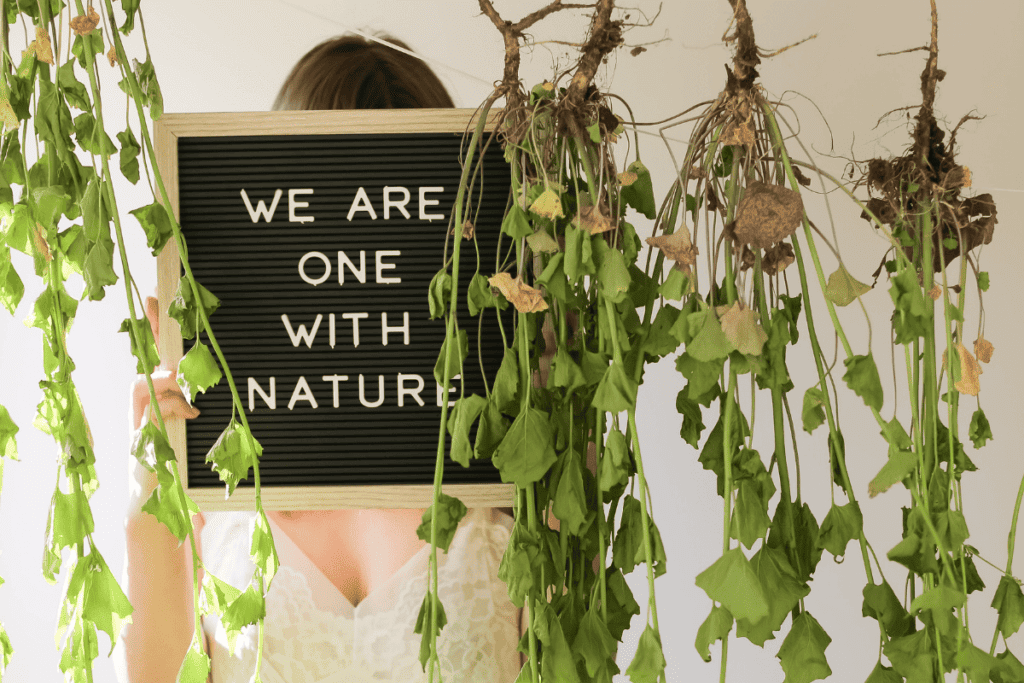 A woman surrounded by plants holding up a letter board that says "we are one with nature."