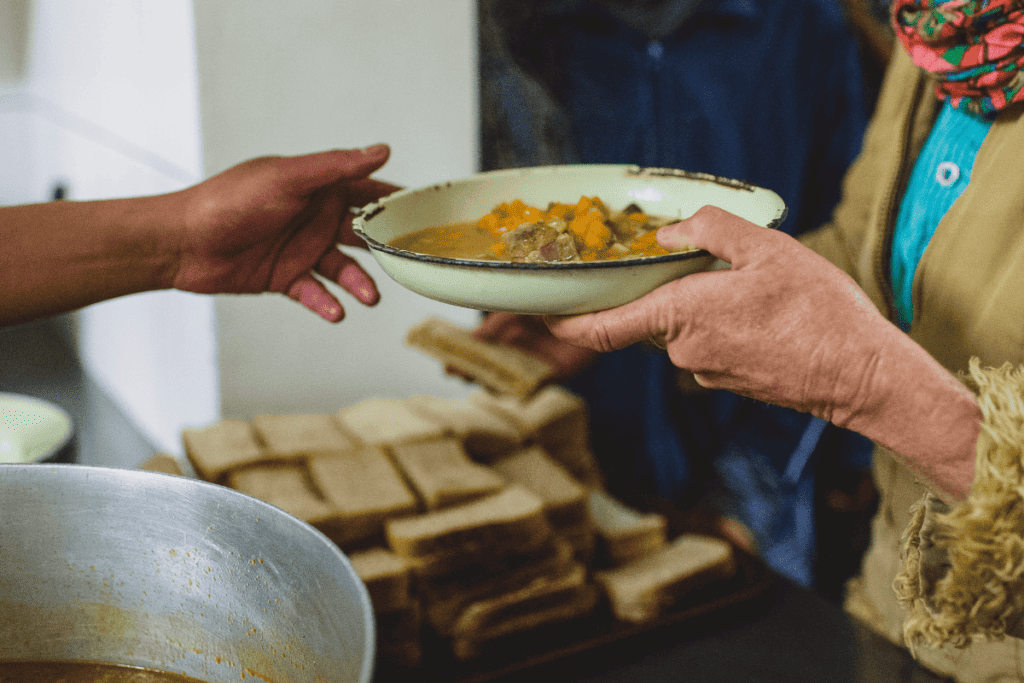 A person at a soup kitchen passing a warm meal to someone.