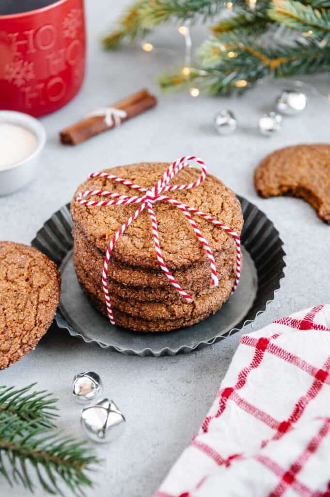 A stack of cookies surrounded by Christmas themed items like fir trees and ornaments.