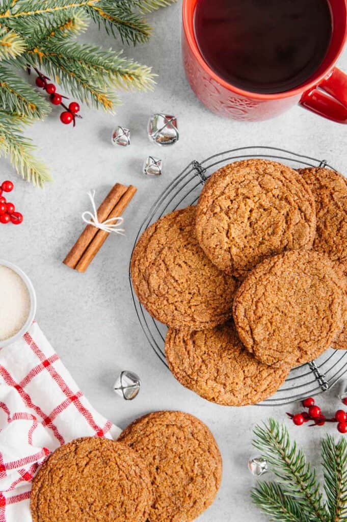 A plate of cookies surrounded by cinnamon, fir tree branches, and a cup of coffee.