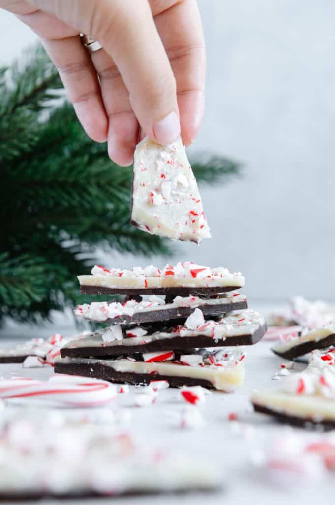 A hand grabbing a piece of peppermint bark from a stack.