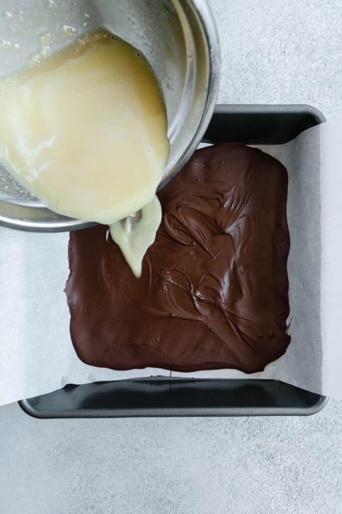 The white chocolate layer being poured over the dark chocolate layer.