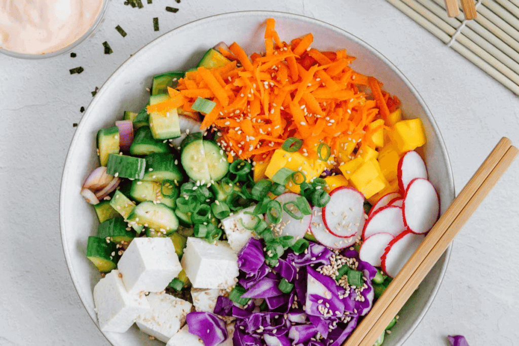A vegan poke bowl with mangos, cabbage, cucumbers, tofu, radish, and carrots.