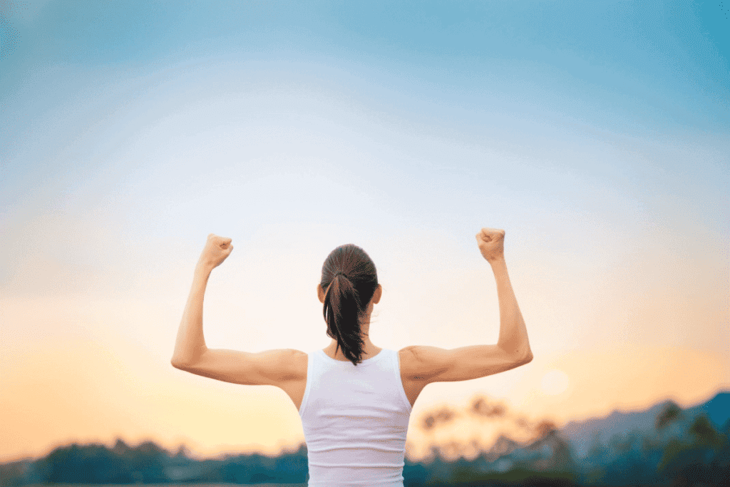 A woman facing a sunrise, showing her strong arms.