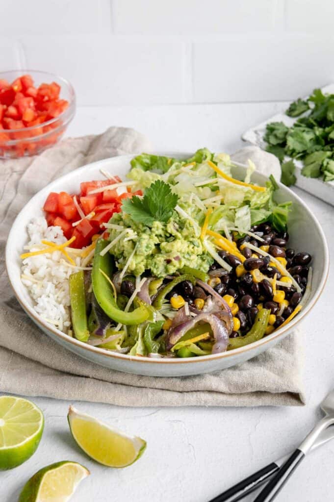 A vegan burrito bowl with lettuce, fajita veggies, guacamole, tomatoes, beans, and corn.
