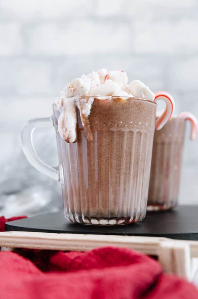 A mug of vegan peppermint hot chocolate dripping with coconut whipped cream.