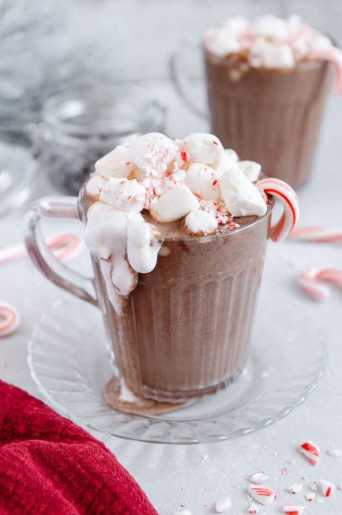 A mug of peppermint hot chocolate overflowing with vegan marshmallows, crushed candy cane, and coconut whipped cream.