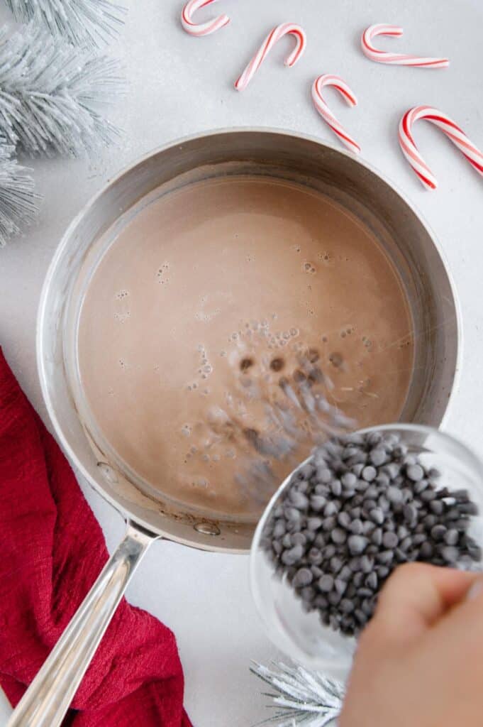 Vegan chocolate chips being poured in the hot chocolate mixture.