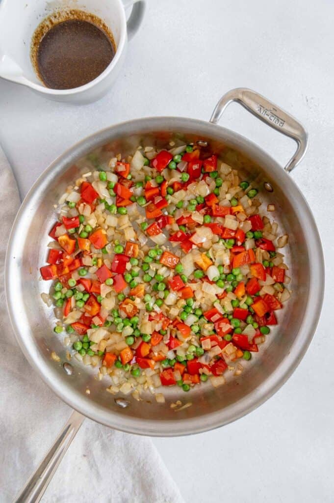 Sautéed red pepper, peas, onions, and garlic in a pan.