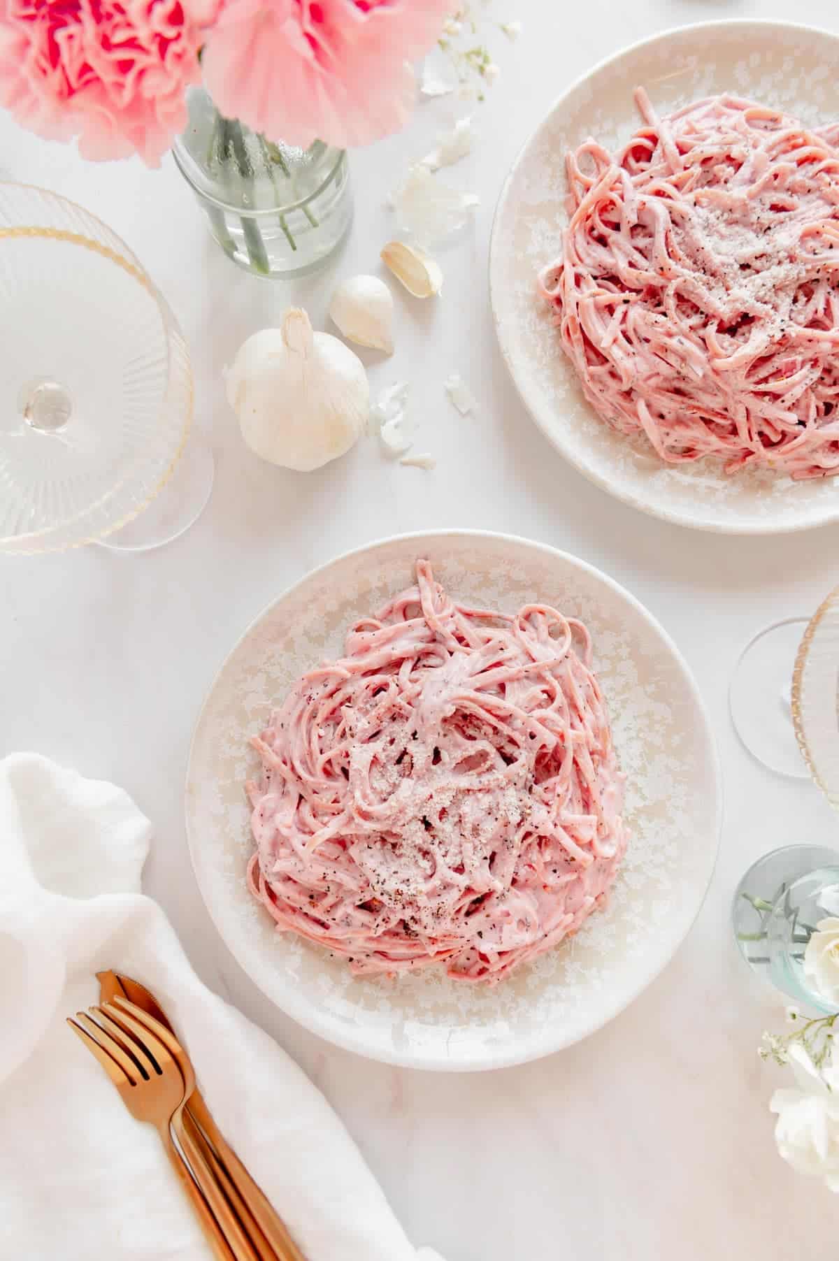 Two plates of pasta with two glasses of wine and flowers.