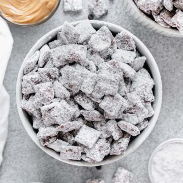 Puppy chow in a bowl surrounded by peanut butter and chocolate chips.