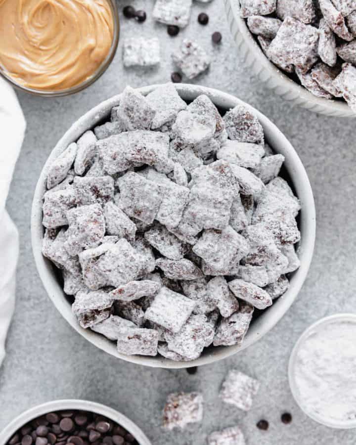 Puppy chow in a bowl surrounded by peanut butter and chocolate chips.