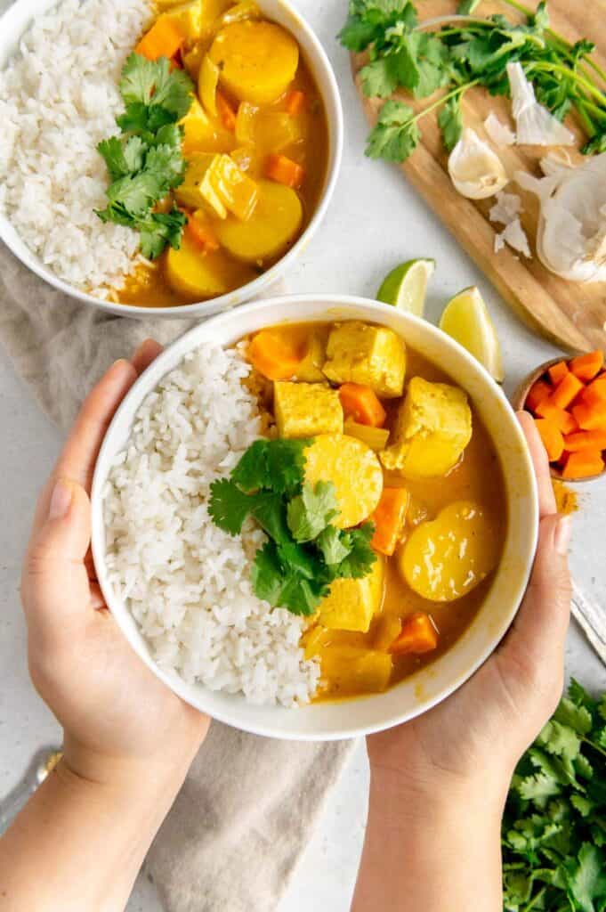 Hands holding a bowl of Thai yellow curry and rice.