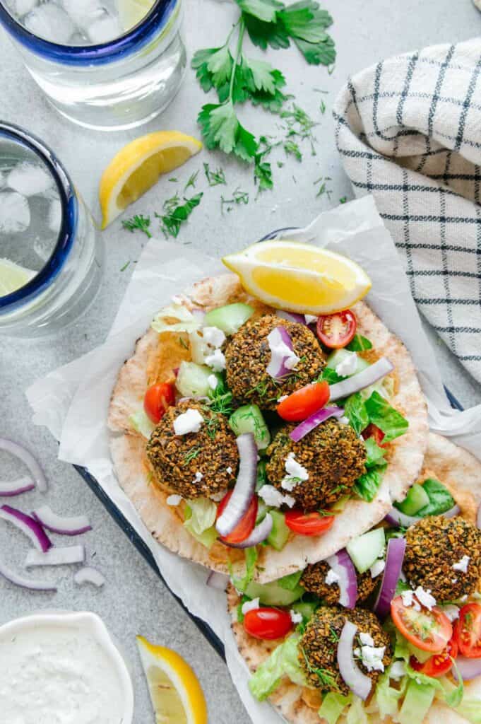 Two falafel sandwiches in a serving tray alongside water and tzatziki sauce.