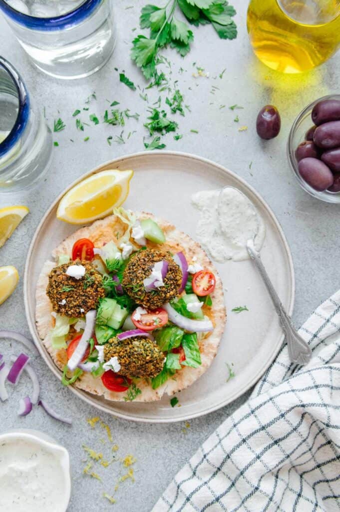 A vegan falafel sandwich on a plate with a lemon wedge and a spoonful of vegan tzatziki.