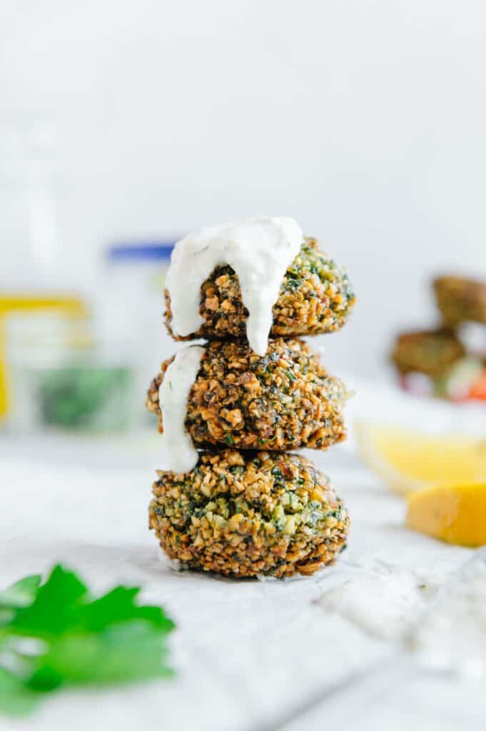 Three vegan falafel balls stacked on top of one another with tzatziki dripping down them.
