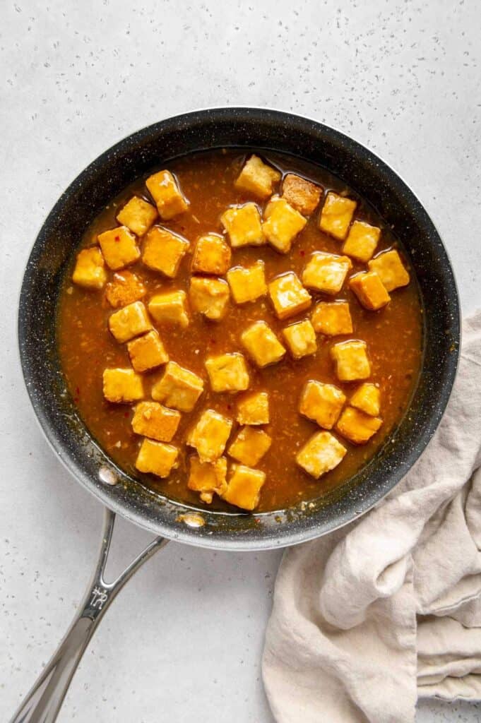 Tofu coated in orange sauce in a non-stick skillet.