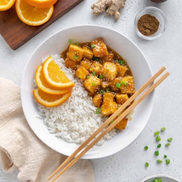 Chopsticks over a bowl of rice and vegan orange tofu.