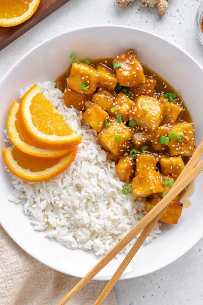 White rice, orange slices, and orange tofu in a bowl.