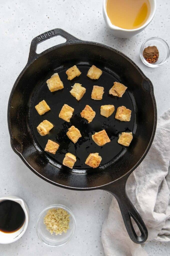 Tofu crisping up in a cast iron skillet.