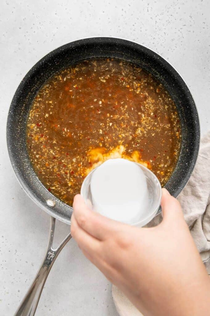 Cornstarch mixed with water being poured into the orange sauce to thicken it.
