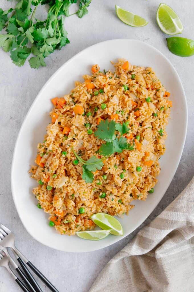 A large platter of Mexican rice garnished with cilantro and limes.