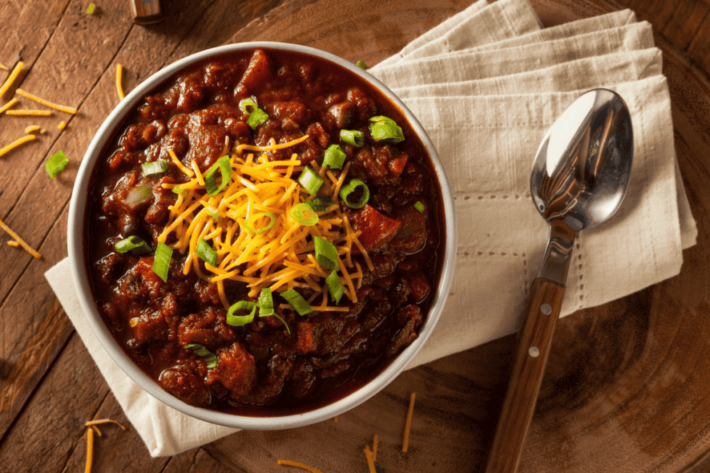 A bowl of chunky chilli topped with cheese and green onions.