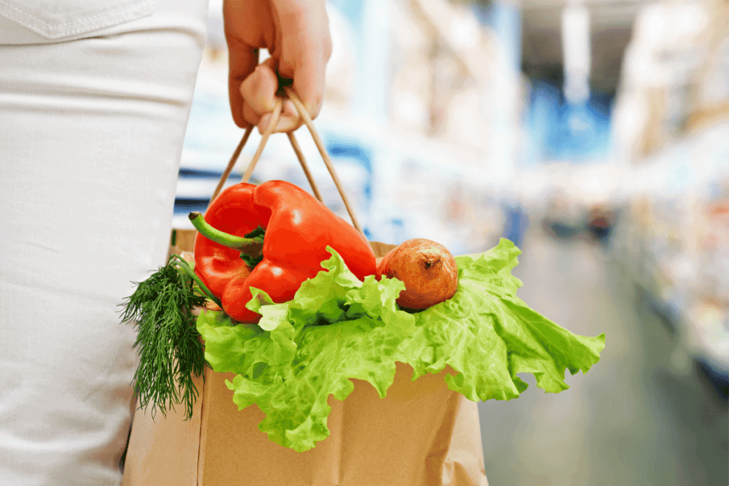 A person holding a grocery bag full of fresh veggies.