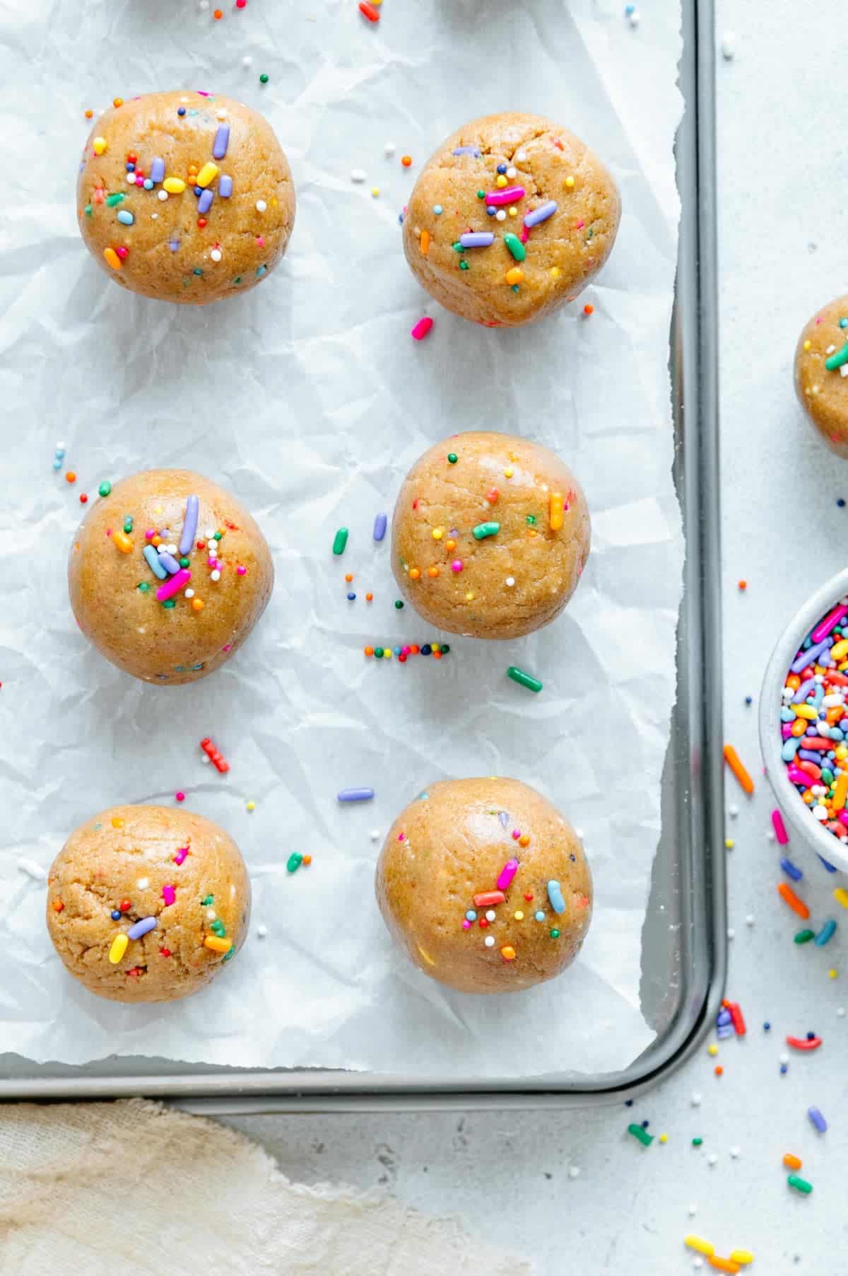 Vegan funfetti protein bites on a parchment lined cookie sheet.