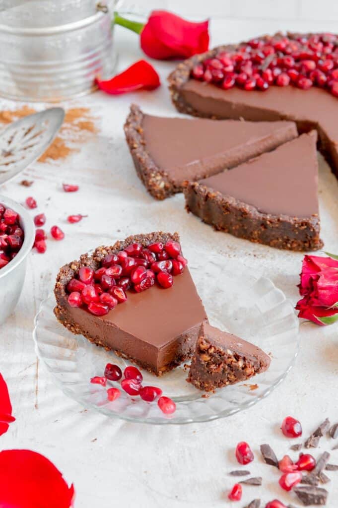 A chocolate tart with pomegranate seeds as a garnish and rose petals scattered around.
