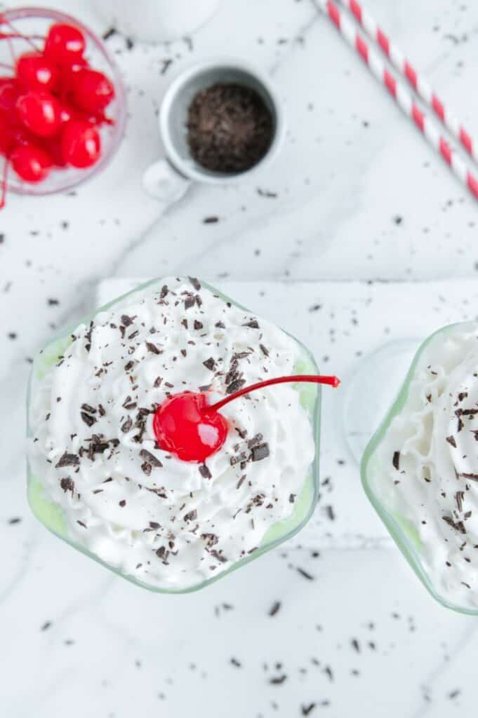 A green milkshake topped with whipped cream, shaved chocolate, and a maraschino cherry.