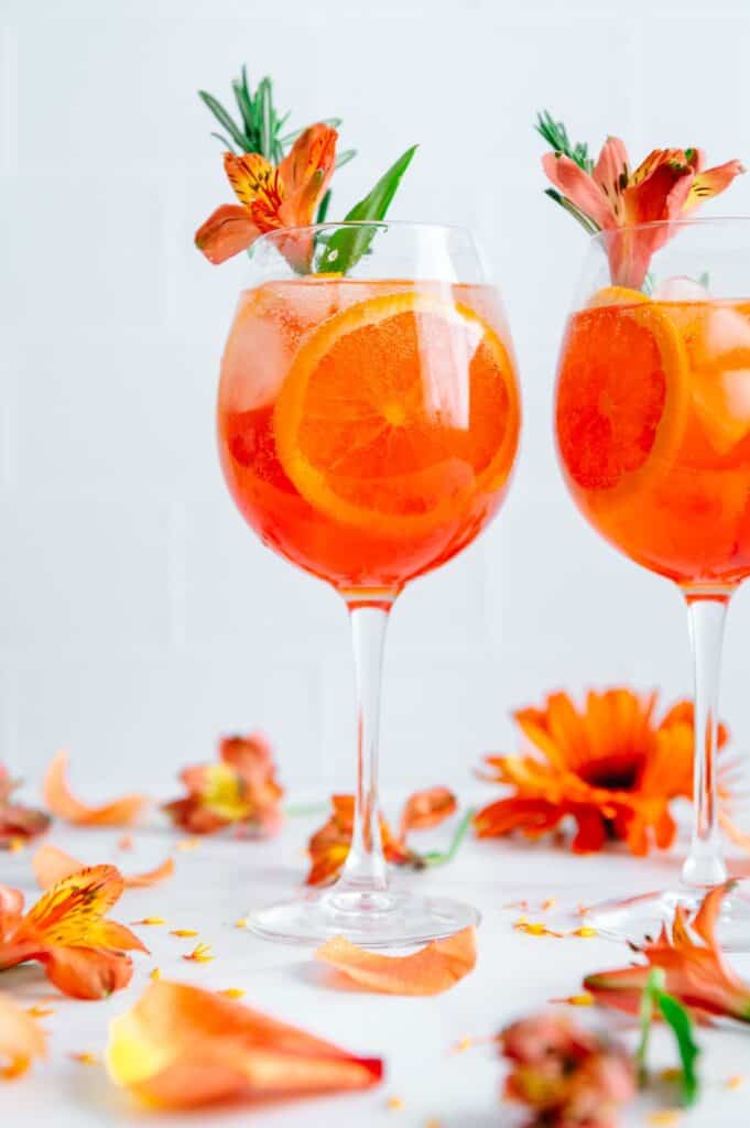 Two Aperol spritz in wine glasses surrounded by flowers.