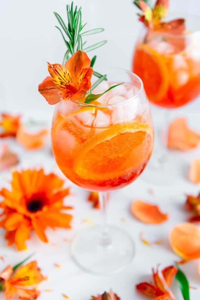 Upclose of an aperol spritz garnished with a fresh flower and fresh rosemary.
