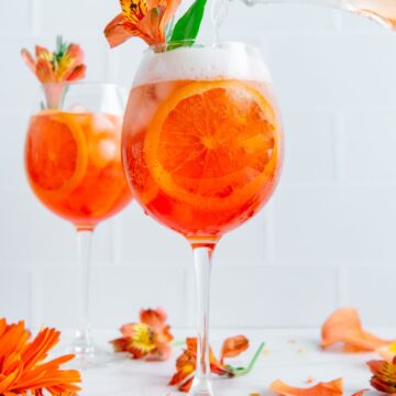 Rosé being poured into a wine glass with Aperol, ice, and orange slices.