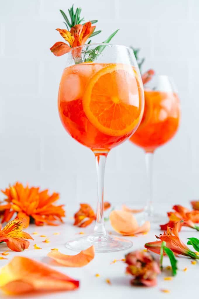 Rosé aperol spritz garnished with a fresh flower and rosemary.