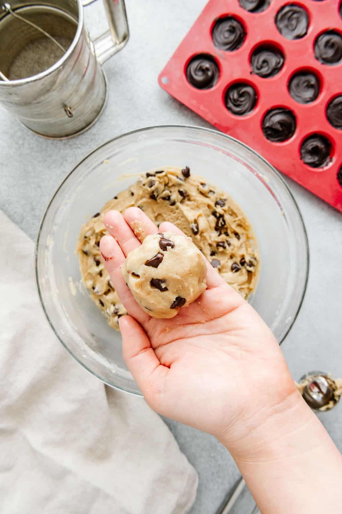 Hands forming cookie dough around frozen nutella disc.