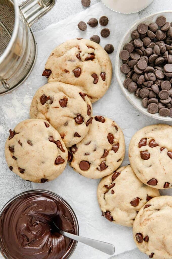 Chocolate chip cookies scattered with chocolate chips and Nutella around.