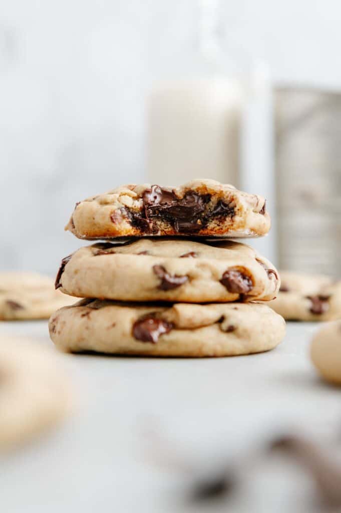 Chocolate chip cookies stacked on top of one another with the top one with a bite taken out of it.