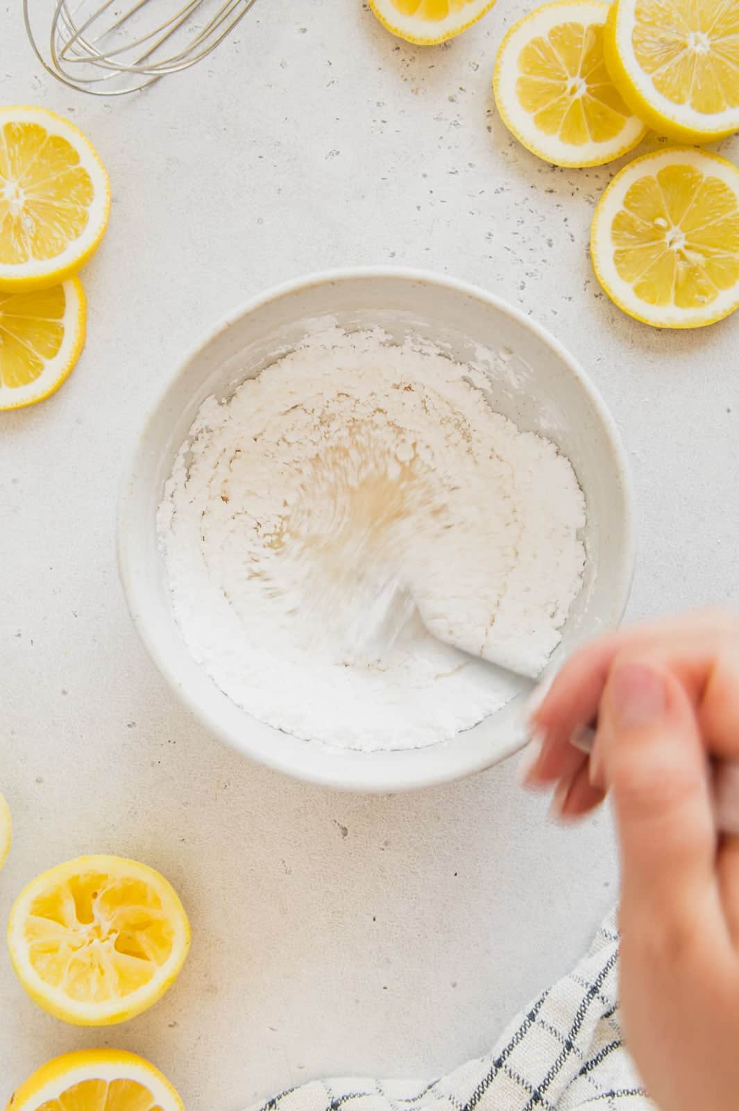 Powdered sugar being mixed with lemon and plant milk to make a glaze.