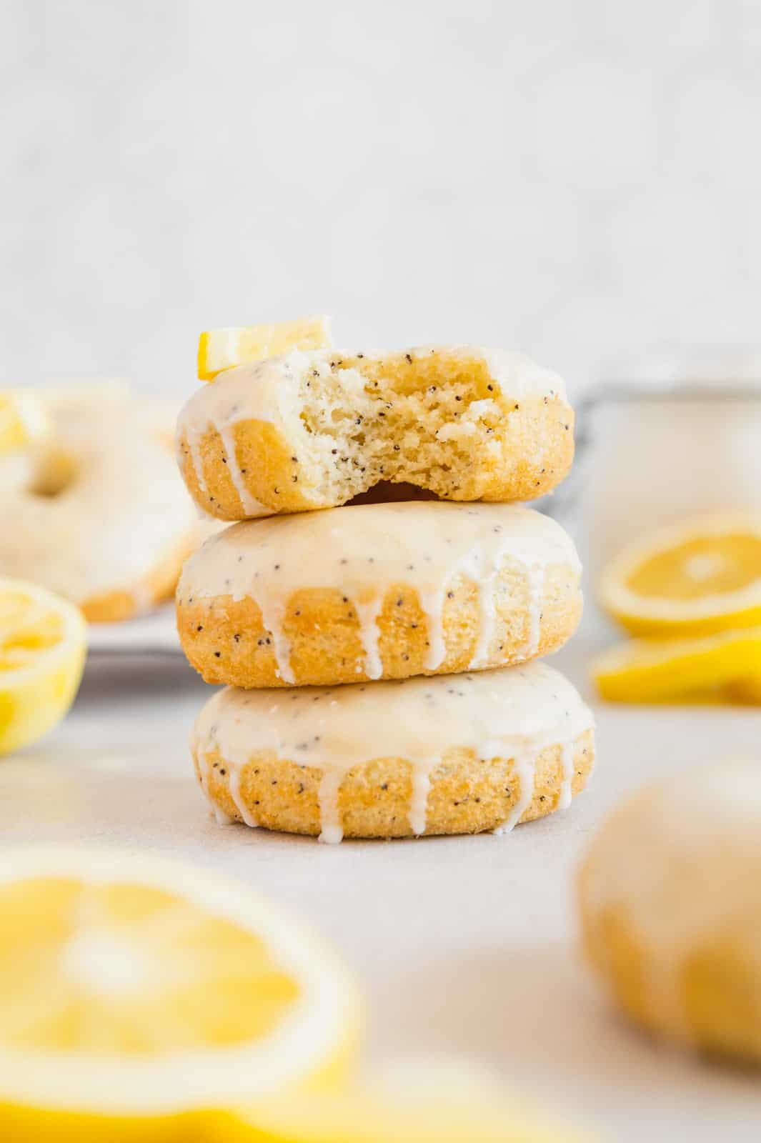 Lemon poppy seed donuts stacked on top of one another with a bite taken out of it.