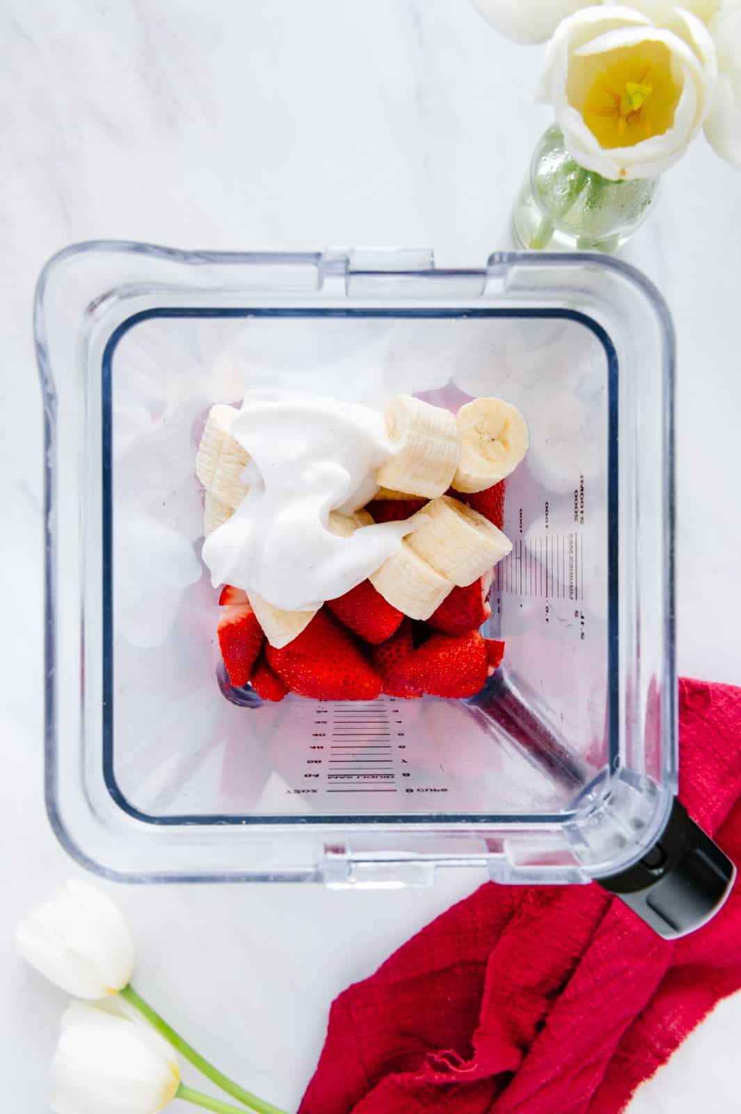 Strawberries, bananas, almond milk, maple syrup, and vanilla yogurt in a blender.