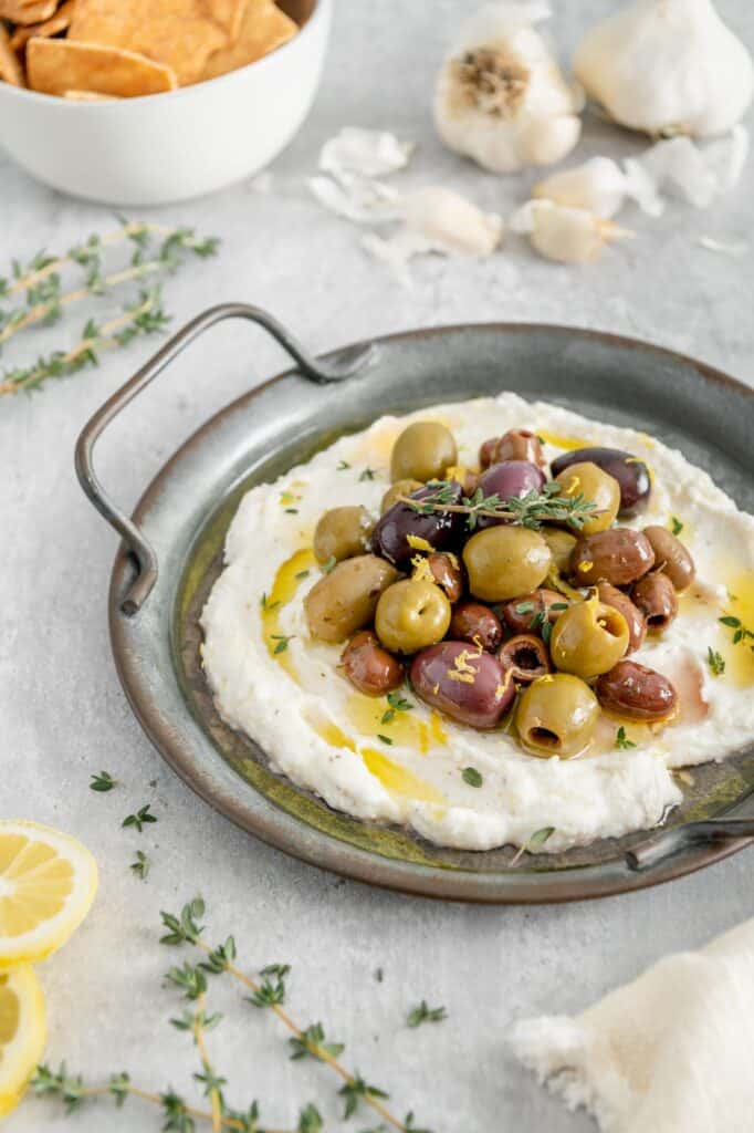 A gourmet vegan whipped feta garnished with olives, thyme, and lemon zest.